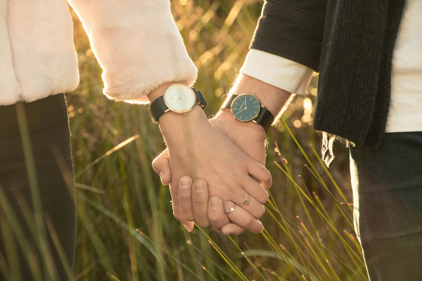 A couple holding hands walking through tall grass at golden hour